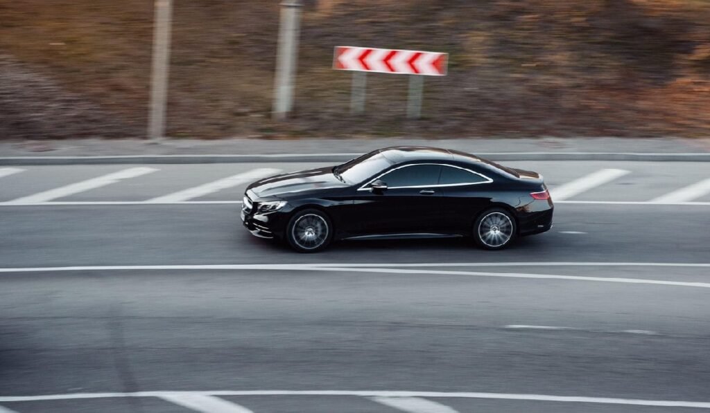 Mercedes coupe negru conducând pe un drum. Profil lateral vedere aeriană a elegant E-class coupe în mișcare la apus de soare.