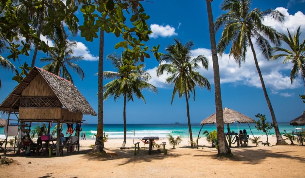 Care este insula tropicală „exact ca Maldive”, tot mai populară printre turiști Plajă tropicală în Palawan, Filipine, cu nisip alb, palmieri, bungalouri tradiționale și apă turcoaz