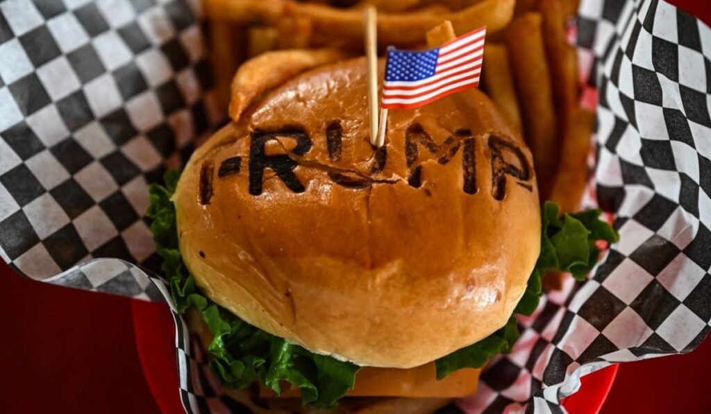 Imaginea arată un burger cu chiflă pe care este inscripționat cuvântul „TRUMP”
