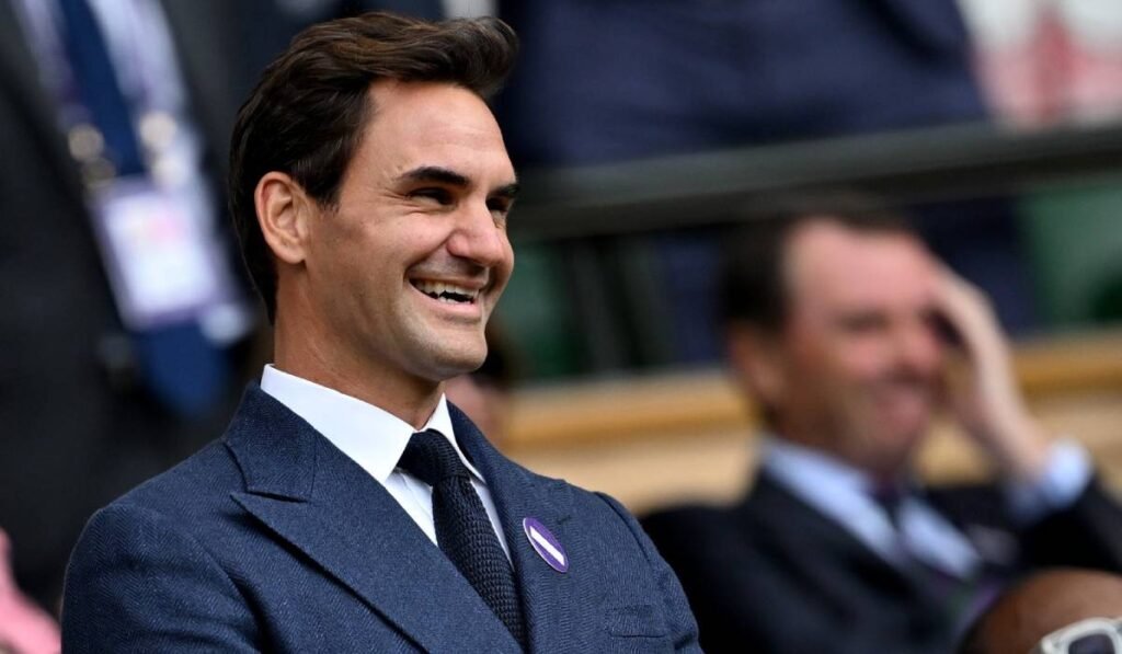 Roger Federer în public, în tribună la un meci de tenis, sportivul poartă un costum albastru
