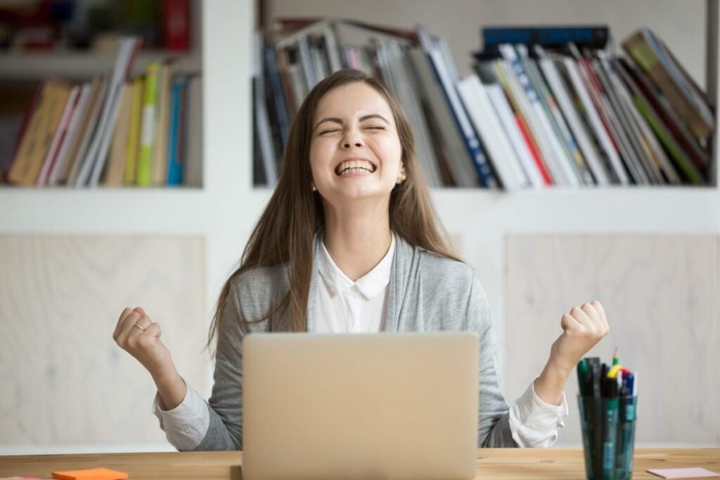 Elevă fericită care râde în fața unui laptop