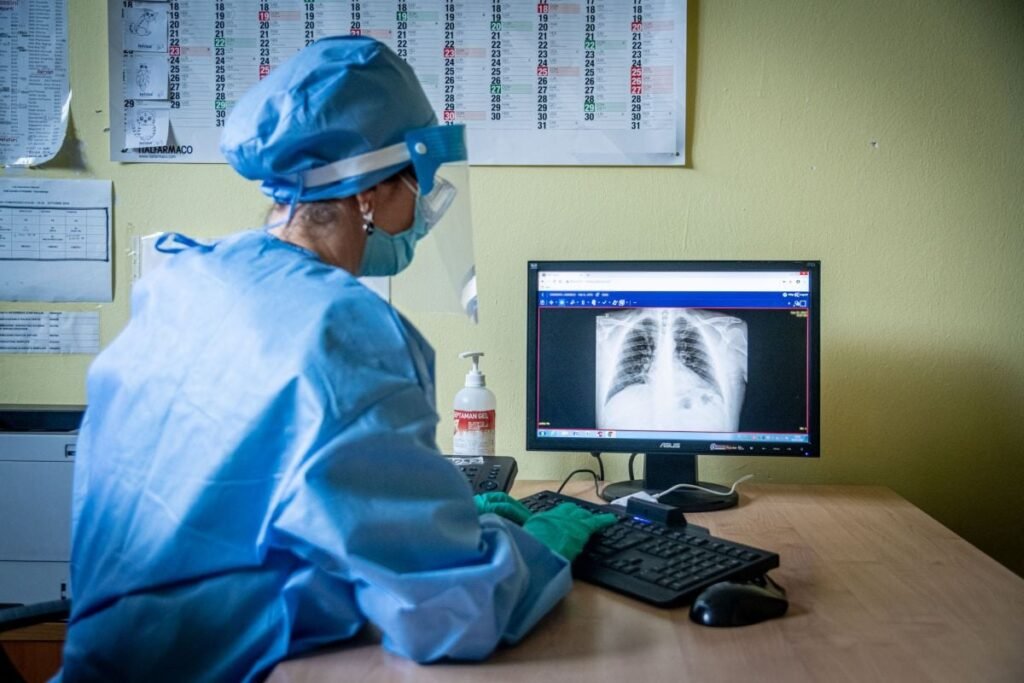 Un cadru medical stă pe scaun și urmărește rediografia unei persoane pe un computer, mai 2020