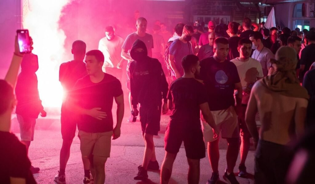 Zeci de tineri, îmbrăcați în tricouri și pantaloni, noaptea, pe o stradă din Novi Sad, cu torțe aprinse pe fundal