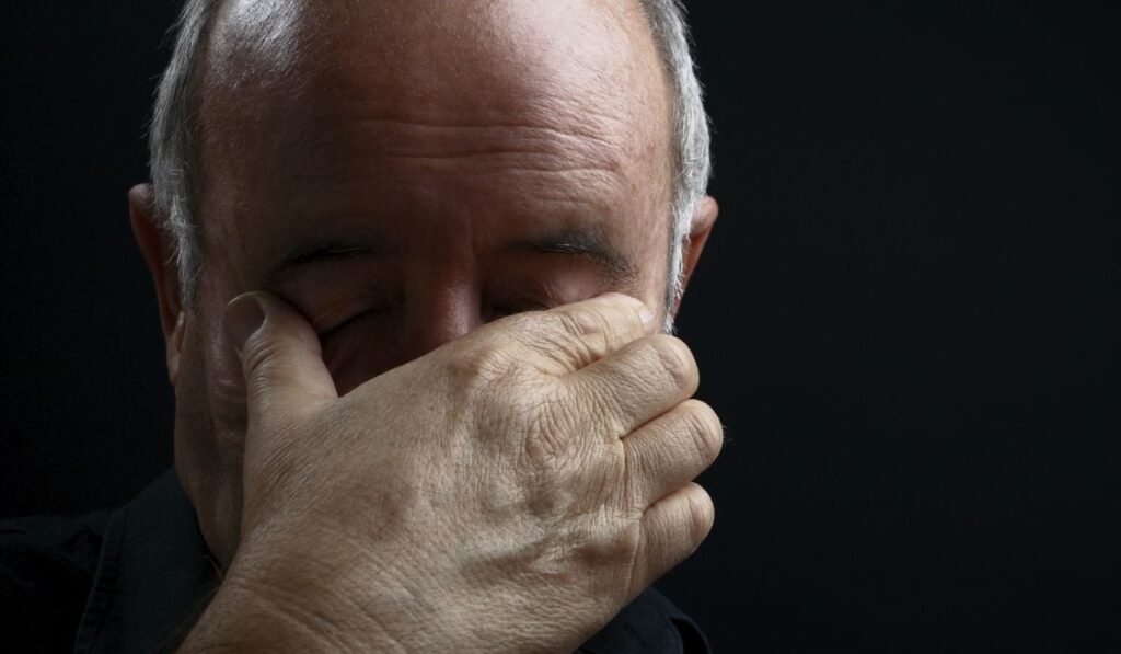 Imagine creativă cu un pensionar, cu chelie, care ține mâna la ochi, pe fundal negru