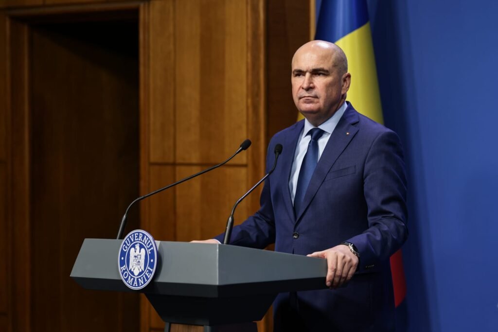 Ilie Bolojan îmbrăcat într-un costum bleumarin, o cămașă albă și o cravată bleumarin, în timpul conferinței de presă de la Palatul Victoria