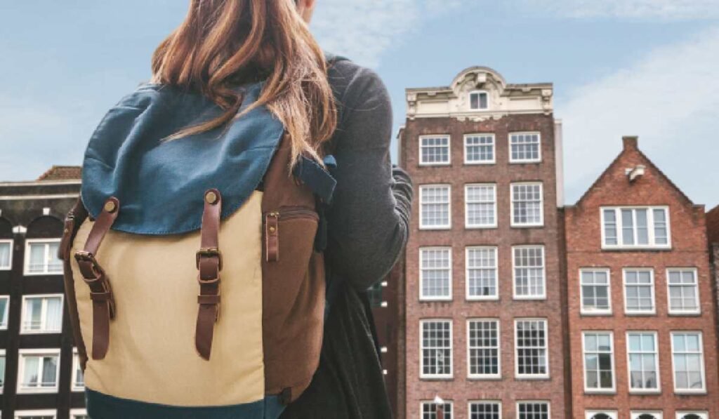 „Te obligă să gândeşti, să aplici şi să argumentezi. În România, şcoala glorifică notele mari” O tânără cu un rucsac se uită la casele tradiționale din Amsterdam, capitala oficială a Țărilor de Jos