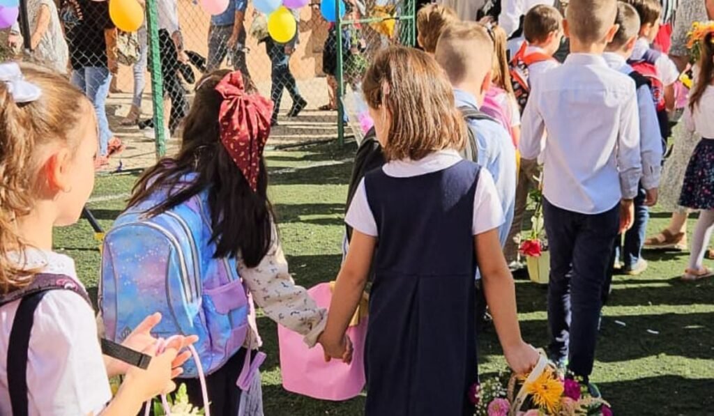 Fotografie cu elevi in uniforma, cu ghiozdane in spate, in prima zi de scoala, tinandu-se de mâna