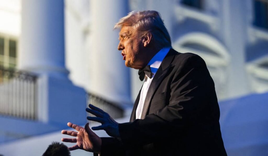 Președintele Statelor Unite, Donald Trump, purtând un frac negru în timp ce ține un discurs la Casa Albă, este fotografiat din profil și gesticulează