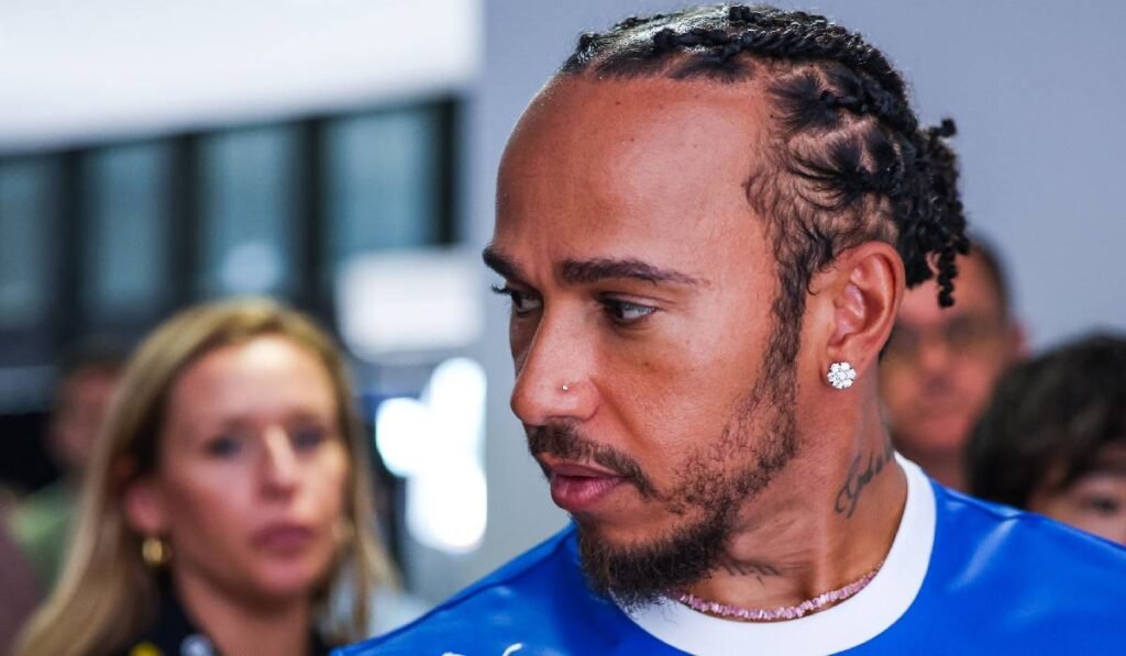 Lewis Hamilton, îmbrăcat într-un tricou albastru în prim plan, privește într-o parte