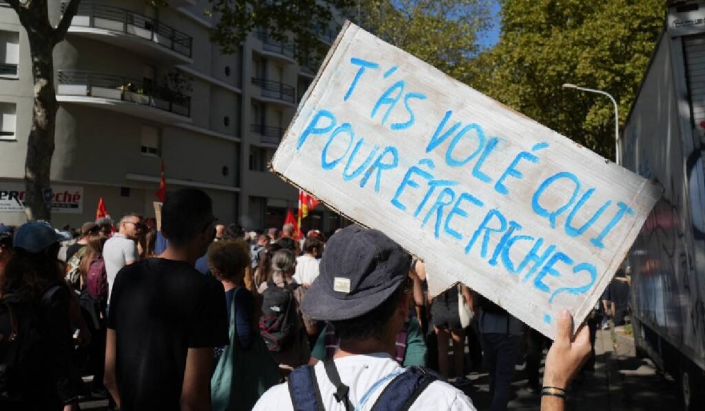 Un protestatar din Franța ține o pancartă pe care a scris: De la cine ai furat ca să te îmbogățești