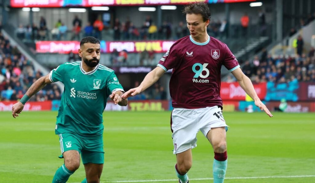 Mohamed Salah (stânga) îmbrăcat în echipament verde aleargă după minge și se contrează cu un adversar pe terenul de fotbal