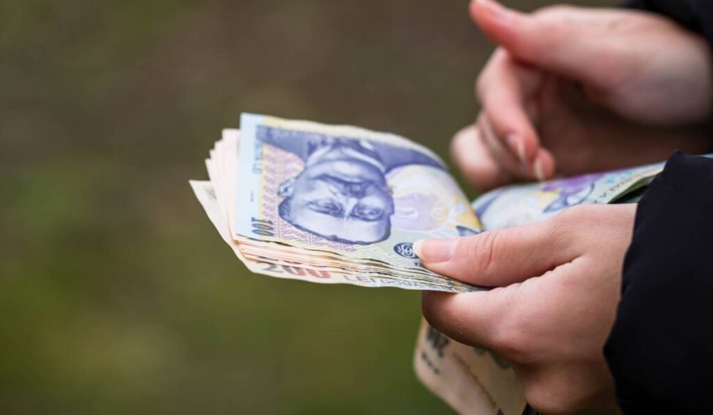 O femeie româncă care numără mai multe hârtii de 100 de lei, îi ține în mână