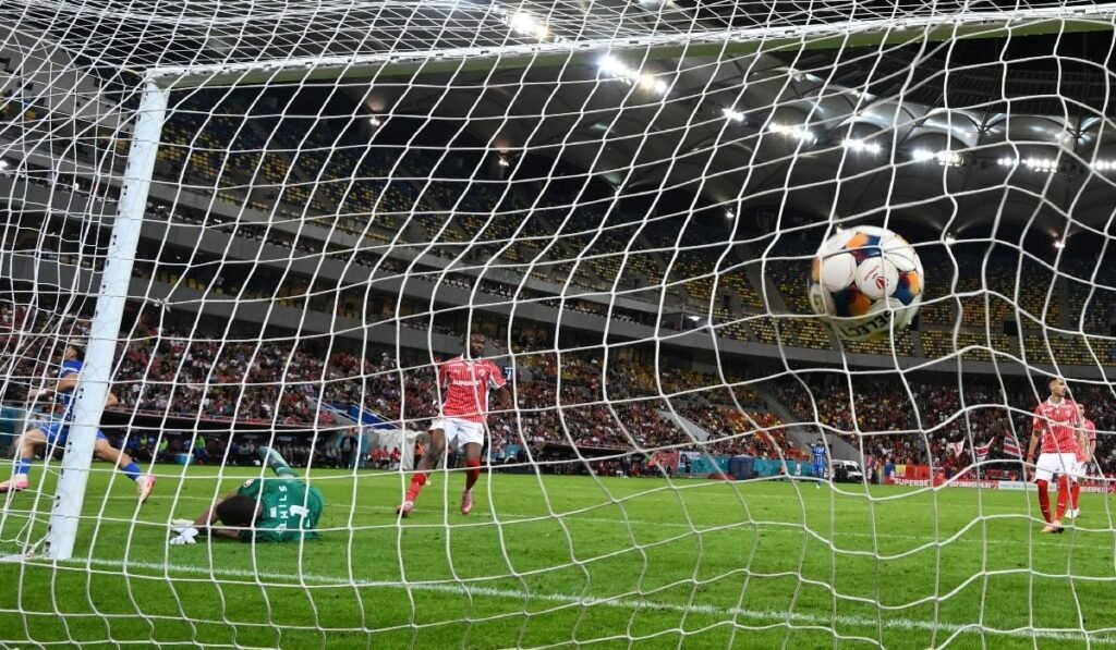 O minge de fotbal intrată în plasă, sub privirile a trei jucători de fotbal