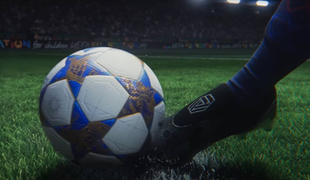 În imagine se vede un picior de jucător care lovește o minge de fotbal aflată pe gazonul unui stadion