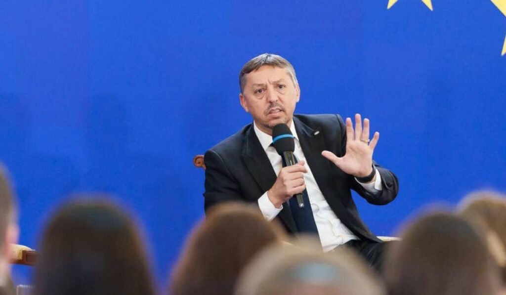 Ministrul Educației, Daniel David, în timpul unei conferințe de presă, vorbește la microfon și explică ceva arătând toate cele cinci degete de la mână