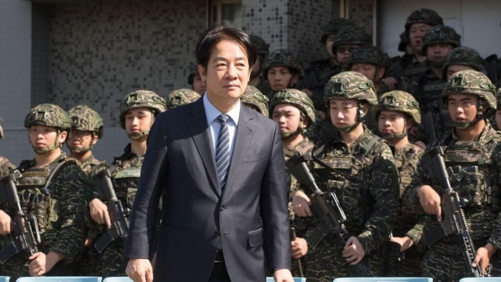 În imagine Președintele Taiwanului, Lai Ching-te, în costum negru si cravată cu multi soldați în uniformă militară și cu arme în spatele său, în inspectează baza Corpului Pușcașilor Marini din Taipei, 21 martie 2025.