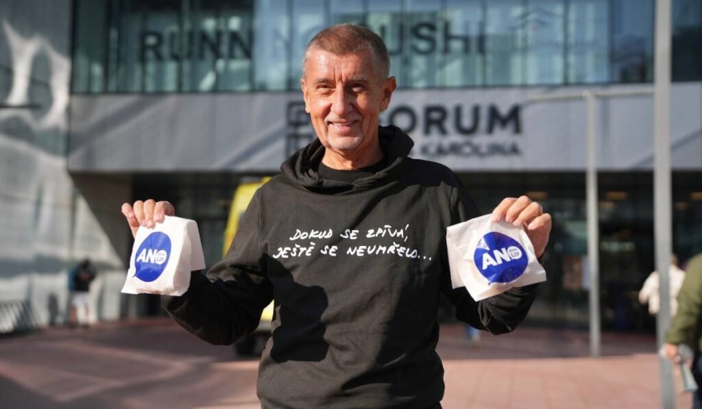 De ce a împărțit Andrej Babiš gogoși în prima zi de vot și ce le promite cehilor dacă revine la putere Miliardarul Andrei Babis. cu un hanorac negru cu un scris alb, cu mainile ridicate si cate o punguta alba cu inscriptie albastra in fiecare mana, a împărțit gogoși în prima zi de vot din Cehia, octombrie 2025