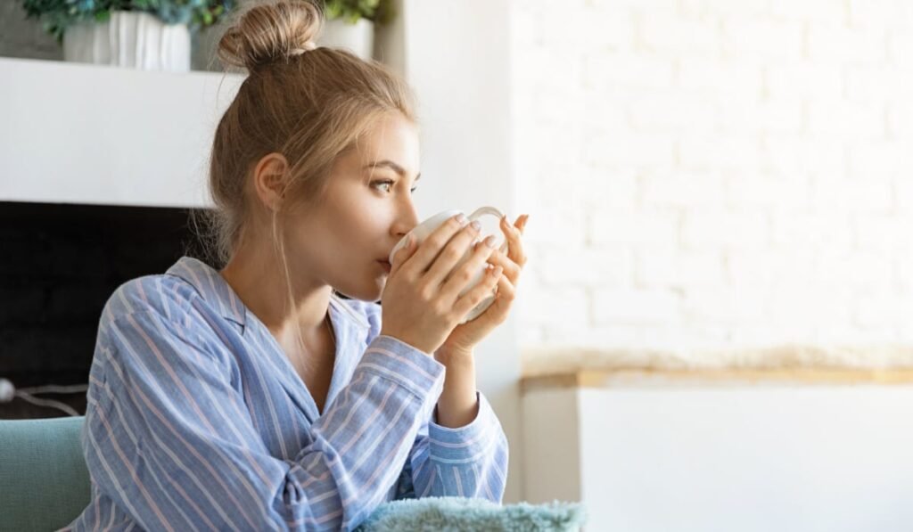 O femeie în pijamale albastre, cu părul strâns în coc. Aceasta bea dintr-o ceașcă albă