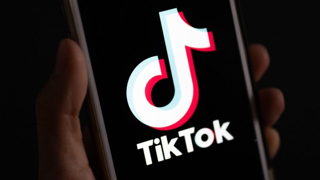 Imagine cu o mână în care se află un telefon mobil pe ecranul căruia este afișat logo-ul TikTok