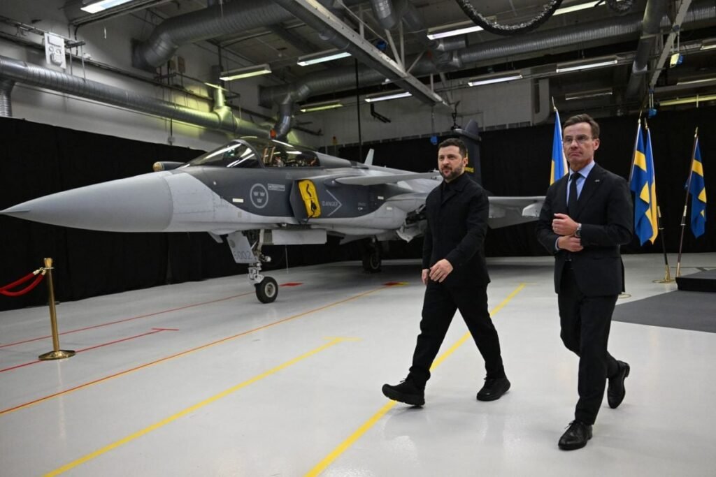 Prim-ministrul suedez Ulf Kristersson și președintele ucrainean Volodimir Zelenski trec pe lângă un avion de vânătoare Gripen, 22 octombrie 2025